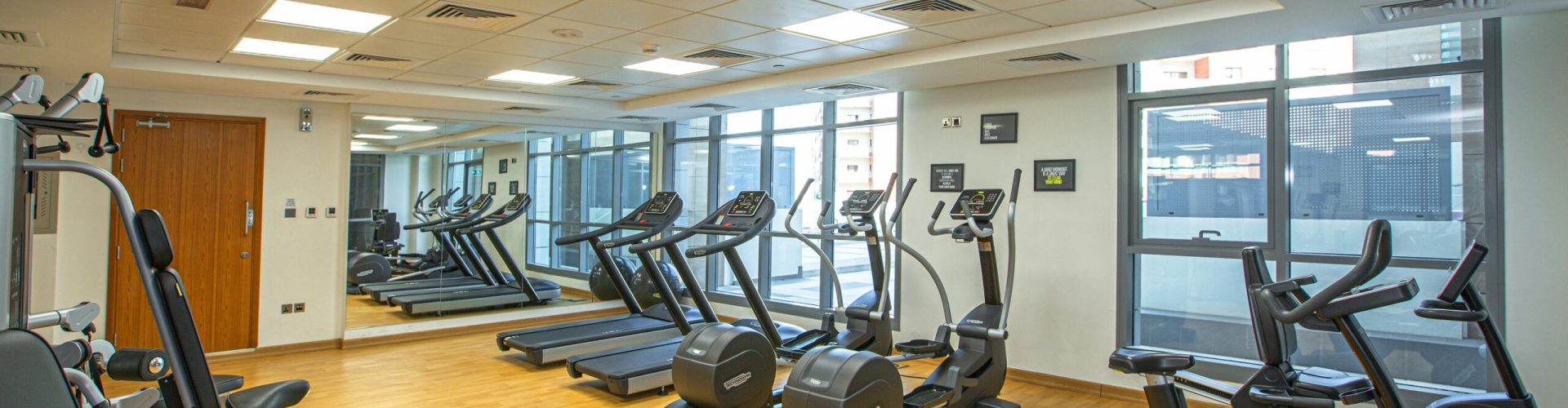 Spacious indoor gym with treadmills, stationary bikes, and exercise equipment on a wooden floor.